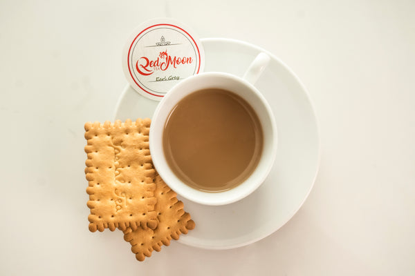 A picture of a teacup full of Earl Grey Tea with milk with a tea saucer with 2 biscuits.